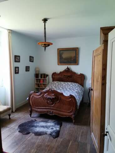 Este quarto aconchegante e com um toque vintage tem uma cama de madeira entalhada, piso de madeira rústico, roupa de cama aconchegante, estante de livros, quadros, tapete de pele de animal e uma luz natural suave.