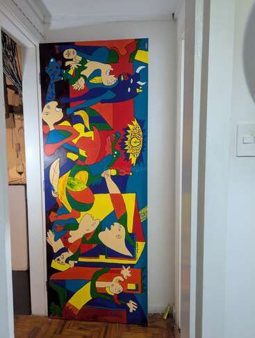 Cette image montre une peinture abstraite colorée représentant des figures humaines et animales déformées, qui rappellent le « Guernica » de Picasso. La peinture trône dans un couloir étroit.