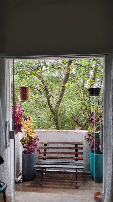 Un balcon confortable avec un banc en bois, entouré de plantes en pot aux couleurs vives, donne sur des arbres verdoyants, créant un havre de paix et de détente à l'extérieur, accessible par des portes vitrées.