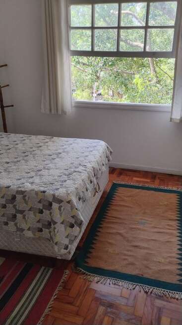 Une chambre confortable avec un couvre-lit à motifs, des tapis colorés, un sol en bois et une grande fenêtre. On aperçoit des arbres verts à l'extérieur, offrant une vue paisible et naturelle.