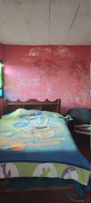 Dieses Bild zeigt ein einfaches Schlafzimmer mit einer Buzz Lightyear-Decke auf einem Bett, roten Wänden mit Zeichnungen, einem Fenster und einem Stuhl neben dem Bett.