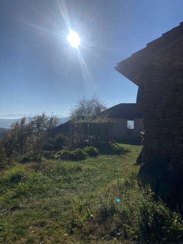Die helle Sonne scheint auf ein rustikales Steinhaus, saftig grünes Gras und Bäume und wirft lange Morgenschatten in eine friedliche ländliche Umgebung.