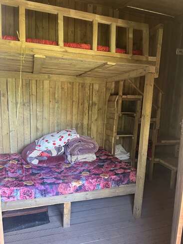 Dieses Bild zeigt ein rustikales Etagenbett aus Holz in einer Hütte, mit geblümter Bettwäsche, Decken, Kissen und Holzwänden, die eine gemütliche, einfache Atmosphäre schaffen.