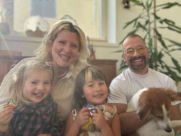 Una familia feliz está sentada junta en casa. Dos niños pequeños sonríen felices junto a sus padres, que están radiantes. Un perro descansa tranquilamente en sus brazos.