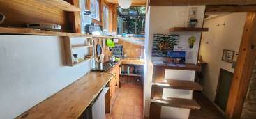 Diese gemütliche Küche hat Arbeitsflächen aus Holz, offene Regale, einen kleinen Herd und große Fenster für natürliches Licht. Eine schwebende Treppe führt zu einem anderen Bereich. Kunst und Utensilien schmücken sie.