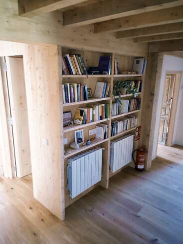 Esta imagen muestra una acogedora habitación de madera con estanterías empotradas llenas de libros y decoración, radiadores debajo y un extintor colocado a la derecha.