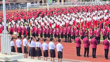 Un grand groupe d'élèves, vêtus d'uniformes, se tient en rangs organisés sur un terrain de sport, participant à une assemblée ou à une cérémonie scolaire formelle en plein air.