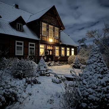 A cozy house glows warmly at night, surrounded by snow-covered trees and bushes. The charming winter scene exudes peacefulness and invites holiday nostalgia and comfort.
