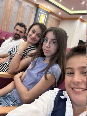 Four people, presumably a family, are sitting in red theater seats. They’re smiling or looking at the camera, appearing happy while waiting for an event.
