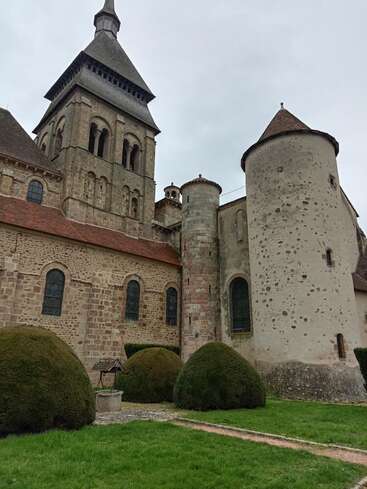 Essa imagem mostra uma igreja antiga de pedra com uma torre alta, torres redondas, janelas em arco e arbustos bem aparados em um gramado verde.