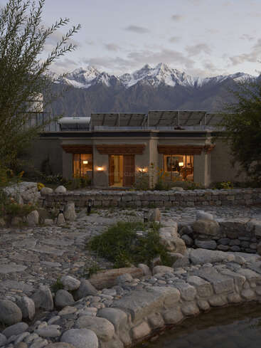 Um tranquilo pátio de pedra leva você a uma casa aconchegante e bem iluminada. As montanhas cobertas de neve formam um cenário de tirar o fôlego sob um céu parcialmente nublado; a beleza natural serena prevalece.