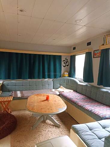 This cozy room has a U-shaped blue couch, wooden table with a candle, soft carpet, turquoise curtains, bookshelf, artwork, and a playful Minion plush toy.