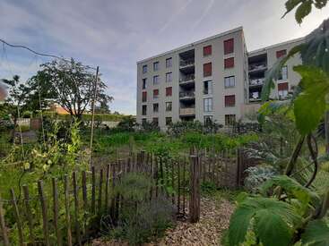 La imagen representa una escena serena de un edificio de apartamentos de varios pisos con un exuberante jardín en primer plano, con diversas plantas y árboles.