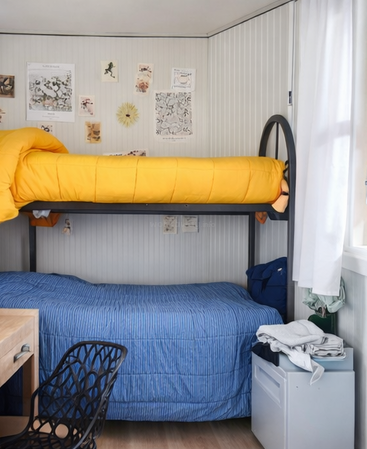Dieses gemütliche Zimmer hat ein Etagenbett mit einer leuchtend gelben Bettdecke oben und einer blauen unten, Wanddekoration, einen Schreibtisch, einen Stuhl und ein Fenster.