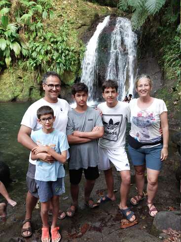 A imagem mostra uma família de cinco pessoas posando em frente a uma cachoeira, com uma vegetação exuberante ao redor, transmitindo uma sensação de alegria e união.
