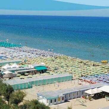 L'image représente une scène de plage avec une grande étendue d'eau, avec une rangée de parasols colorés et des bâtiments le long du rivage.