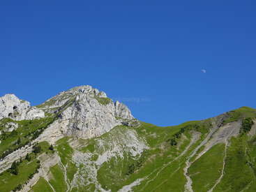 The image depicts a mountainous landscape with a clear blue sky, featuring a prominent rocky peak and lush greenery, set against a serene natural backdrop.
