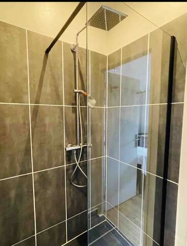 This image shows a modern shower with dark, large wall tiles, a glass enclosure, a rainfall showerhead, and a handheld shower attachment in a clean bathroom.