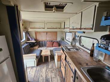 L'intérieur confortable de ce camping-car comprend une cuisine compacte avec un plan de travail en bois, une cuisinière, un évier, des sièges rayés, une petite table, des placards, des coussins et un sol en bois rustique.