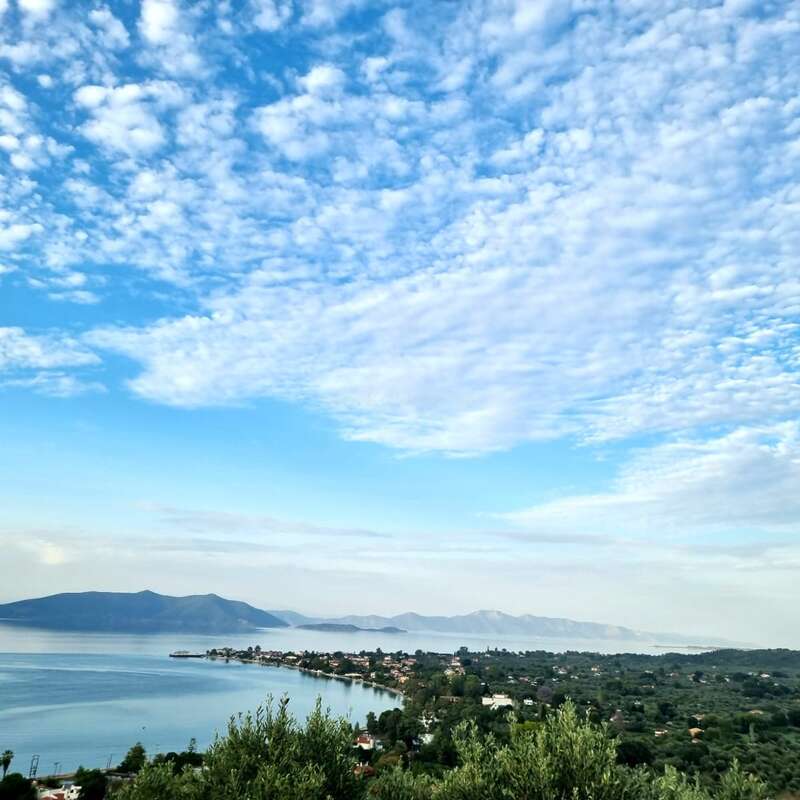 Un magnifique paysage côtier composé d'une eau bleue calme, d'une végétation luxuriante, de montagnes lointaines, de maisons pittoresques et d'un ciel magnifique parsemé de nuages blancs cotonneux par une journée ensoleillée.