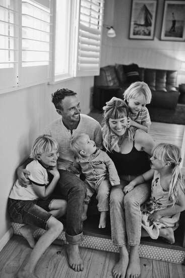 Une joyeuse famille de six personnes est assise à l'intérieur. Des parents souriants et quatre enfants joyeux partagent un moment de bonheur et de jeu dans cette photo confortable en noir et blanc.