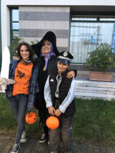 Trois personnes costumées posent en plein air. L'une est habillée en sorcière, une autre en policier et une autre en orange avec une épée et un seau à citrouille.