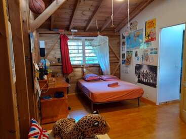Este quarto aconchegante tem um interior em madeira, cama com mosquiteiro, escrivaninha, pôsteres, mapa-múndi, bola de basquete, bichinho de pelúcia, globo terrestre, cortina vermelha e decorações nas paredes.