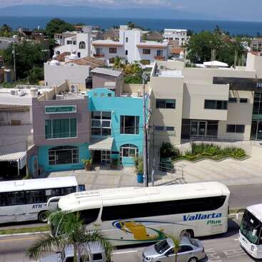 La imagen muestra una hilera de edificios con una carretera que pasa por el medio, con una mezcla de propiedades residenciales y comerciales, y algunos árboles y espacios verdes diseminados.