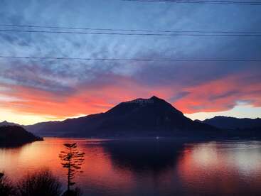 La imagen representa una serena escena lacustre al atardecer, con una majestuosa montaña de fondo y vibrantes tonos rosas y naranjas reflejados en la superficie del agua.