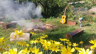 The image depicts a serene outdoor setting with a fire pit, surrounded by trees and a body of water, evoking a sense of tranquility and natural beauty.
