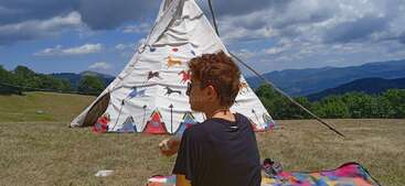 The image depicts a serene scene of a person standing in front of a large tent, with a body of water and trees visible in the background, evoking a sense of tranquility and relaxation.