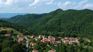 Ein malerisches Dorf mit Häusern mit roten Dächern, eingebettet inmitten üppig grüner Hügel. Die Landschaft besticht durch sanfte Hügel, einen klaren Himmel und eine ruhige, friedliche Natur.