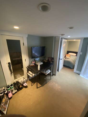 Voici une chambre confortable équipée d'un petit bureau, d'une télévision, d'un meuble à chaussures, d'une armoire et d'un lit bien fait, avec des peluches dans une alcôve. L'éclairage est chaleureux.