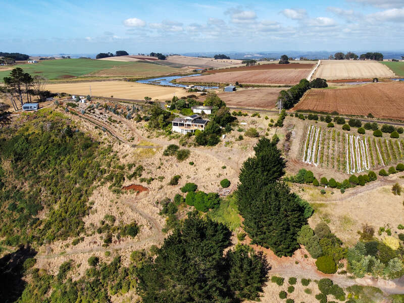 Esta imagem mostra uma paisagem rural com uma casa em uma colina, cercada por campos, terras agrícolas, árvores, jardins e um rio que serpenteia pelo campo.