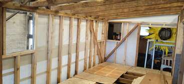 This image shows the interior framework of a wooden structure under construction, with exposed beams, partially completed floor, and tools in the background. Decorations are visible.