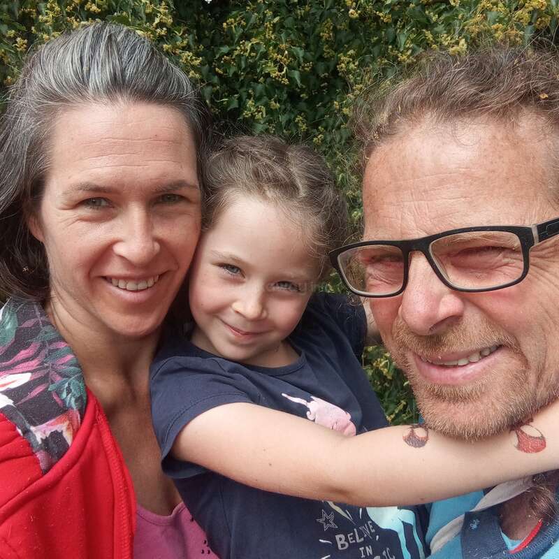 Une famille heureuse de trois personnes - la mère, le père et la fille - sourit en plein air, entourée de verdure, profitant d'une journée ensoleillée et créant de beaux souvenirs.