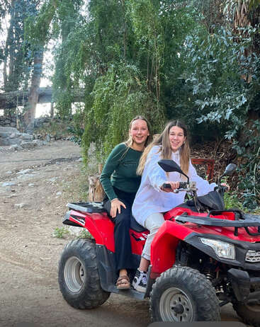Deux jeunes femmes sont joyeusement assises sur un VTT rouge dans un cadre extérieur semblable à une forêt, entouré d'arbres verdoyants, souriant et profitant de leur aventure.