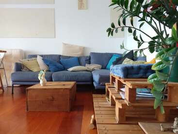 Un salon confortable est composé d'un canapé sectionnel bleu avec des coussins assortis, d'une table basse en bois, de meubles en palettes, d'une plante verte, d'un sol en bois et d'une décoration murale minimale.