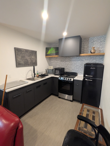 Dies ist eine moderne, kompakte Küche mit schwarzen Schränken, einer Spüle, einem Herd und einem Kühlschrank im Vintage-Stil. Ein roter Stuhl und ein Holztisch sind ebenfalls zu sehen.