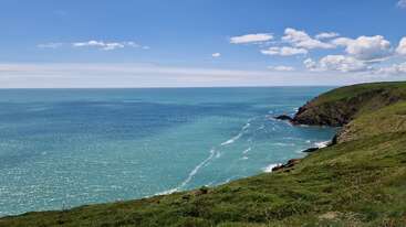 Une superbe scène côtière avec une mer d'un bleu éclatant, des falaises verdoyantes et des nuages épars dans un ciel ensoleillé, créant une atmosphère paisible, pittoresque et rafraîchissante.