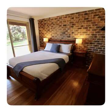 Ein gemütliches Schlafzimmer mit einer Akzentwand aus Backstein, Holzböden, einem Holzbett mit weißer und blauer Bettwäsche, zwei Nachttischen mit Lampen und einem großen Fenster.