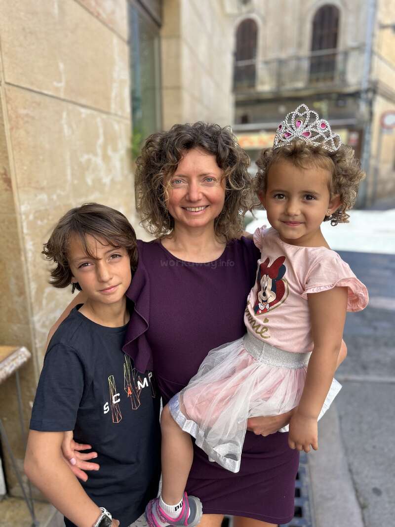 The image depicts a woman posing with two children, a boy and a girl, on a city street, showcasing a tender moment between the trio.