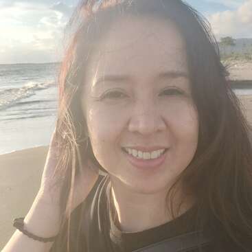A woman smiles at the camera while standing on a beach during sunset. The ocean waves and sandy shore create a serene, pleasant, and relaxed atmosphere around her.