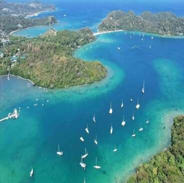 A stunning aerial view of a turquoise cove with boats anchored, lush green hills, clear waters, ideal for swimming, snorkeling, diving, sailing, and hiking adventures.