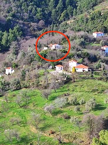 A imagem mostra uma encosta verdejante salpicada de casinhas. Uma casa branca com telhado vermelho, circulada em vermelho, destaca-se entre as árvores.