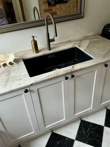 Un lavabo de salle de bains moderne avec une vasque noire, un meuble blanc et un comptoir en marbre. Il y a un robinet métallique, un distributeur de savon, un décor de coquillages et des carreaux à carreaux noirs et blancs.