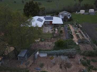 Dieses Bild zeigt ein ländliches Haus mit Sonnenkollektoren, umgeben von Gärten, Hochbeeten, Schuppen, eingezäunten Flächen, Bäumen und grünen Feldern auf dem Lande.