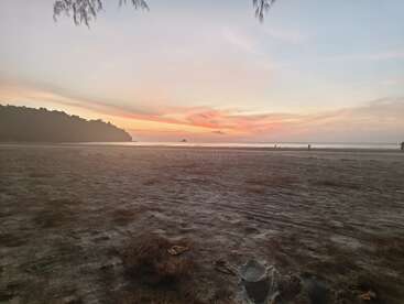 Das Bild zeigt eine heitere Strandszene bei Sonnenuntergang mit einem Sandstrand, einem Gewässer und einer entfernten Insel, die ein Gefühl der Ruhe hervorruft.