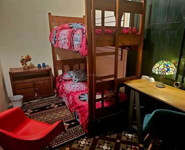 This cozy room features wooden bunk beds with bright red floral bedding, a patterned rug, a red chair, a desk with a stained-glass lamp, and dresser.