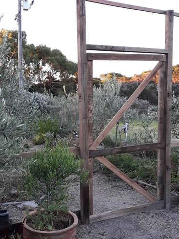 The image depicts a rustic wooden gate in a garden, with a potted plant in the foreground and a gravel path leading to a serene outdoor setting.